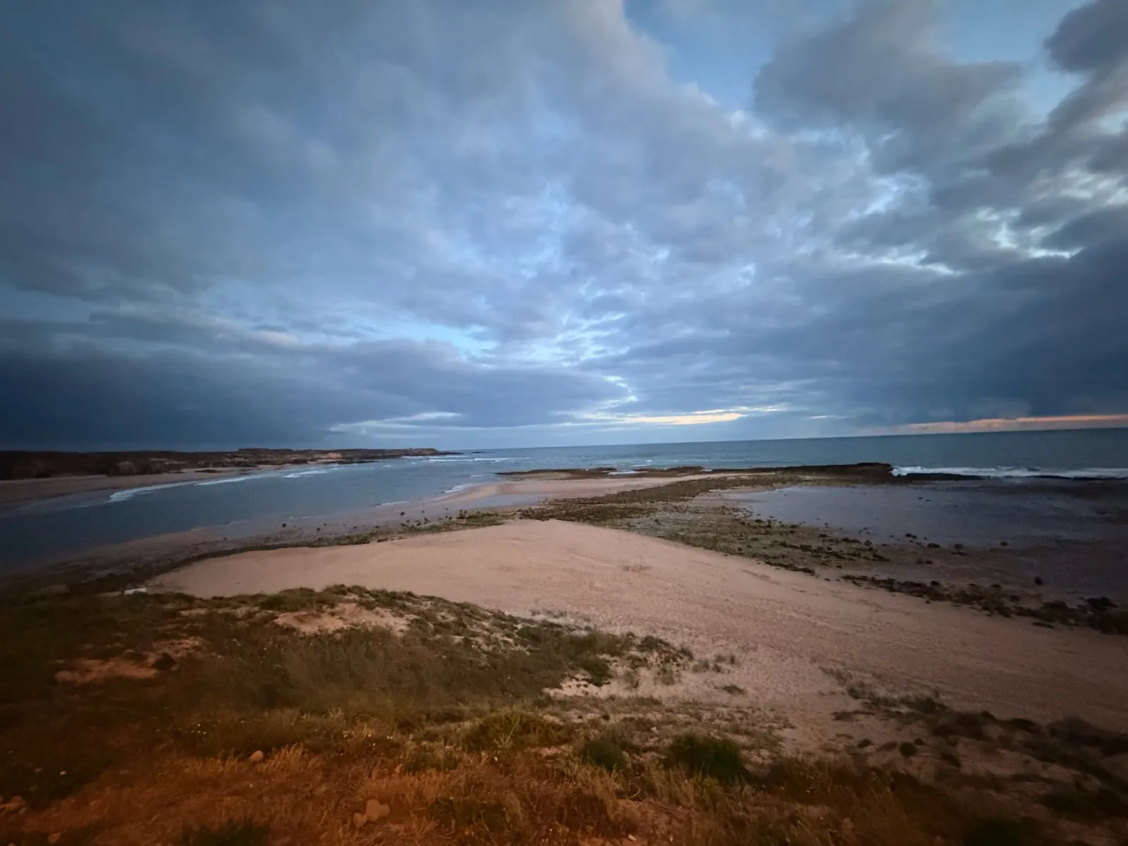 Dramatic cloudy sky over a quiet Alentejo estuary at dusk, sand bars and still water stretching to the horizon