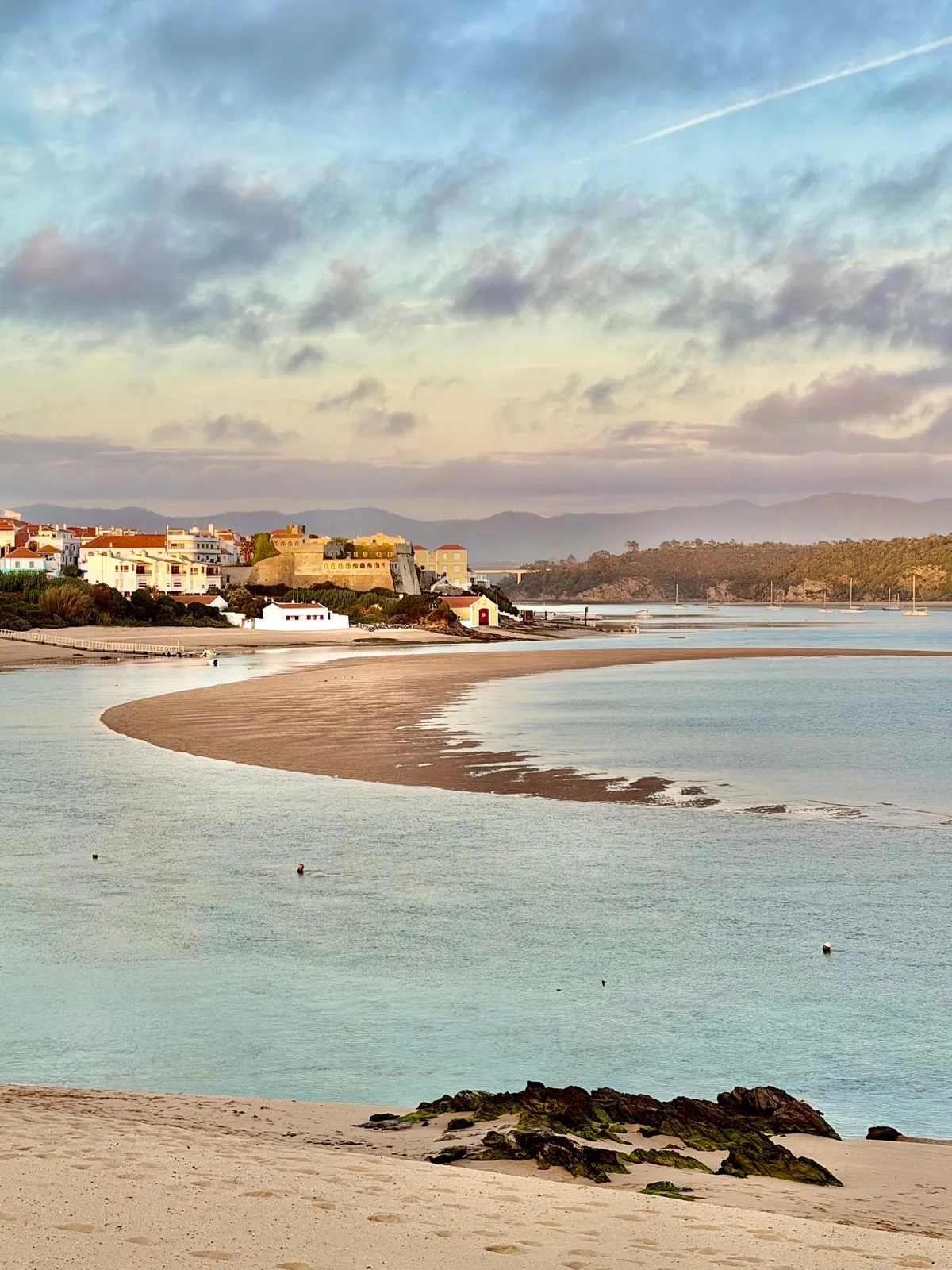 Coastal town with a medieval castle overlooking a curving sandy beach and calm estuary at golden hour