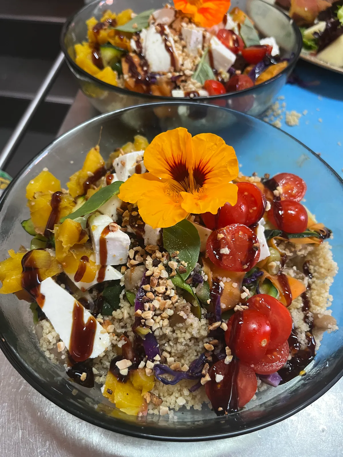 Vibrant grain bowl topped with cherry tomatoes, feta, crushed nuts and an edible nasturtium flower