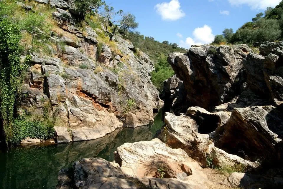 Rocky gorge with layered stone formations surrounding a still emerald pool in the Alentejo countryside