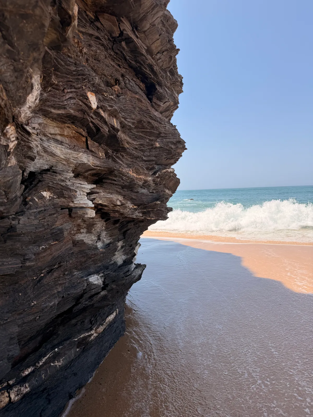 Jagged dark rock outcrop in the foreground with a sandy beach and turquoise Atlantic surf stretching behind