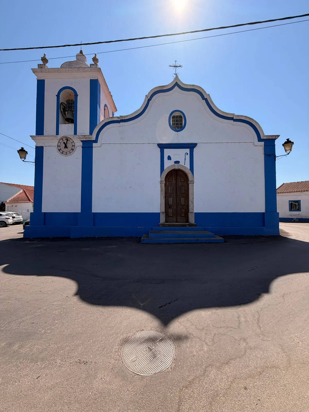 The whitewashed São Luís village church with bright blue trim, a scalloped baroque gable, wooden door and a bell tower with a clock, standing against a clear blue sky