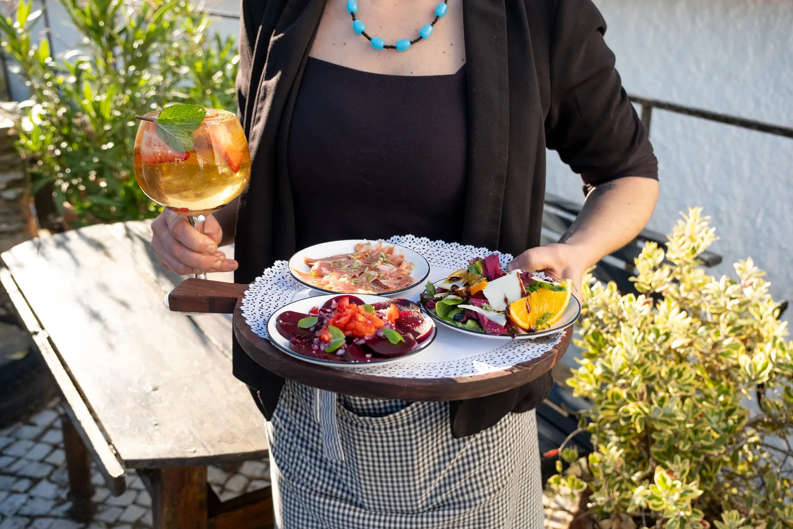 Woman carrying a wooden tray of colourful plates and a sangria on a sunny Portuguese terrace